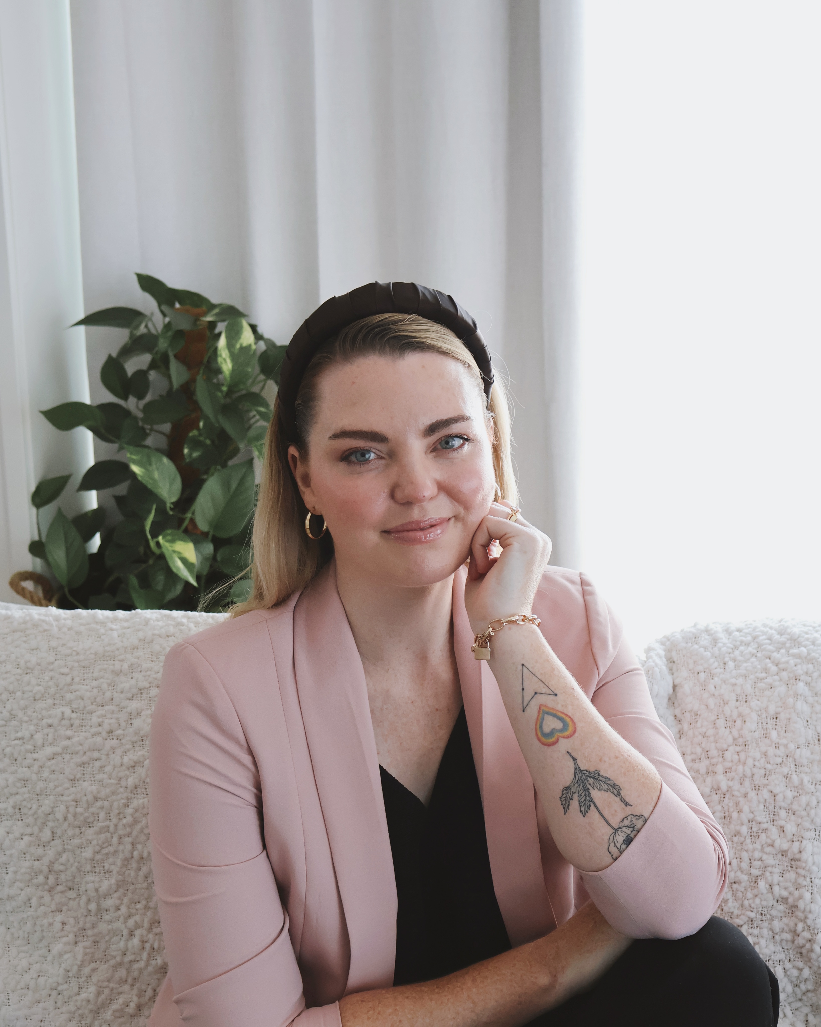 Amy Thunig sits looking into the camera and smiling. She is wearing a light pink blazer and black headband. 