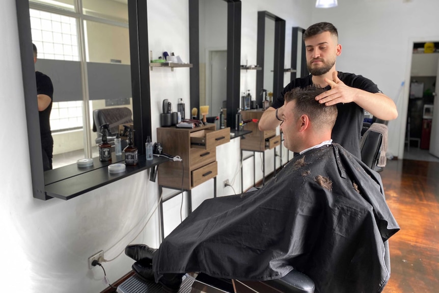 A barber cutting a man's short brown hair in a chair.