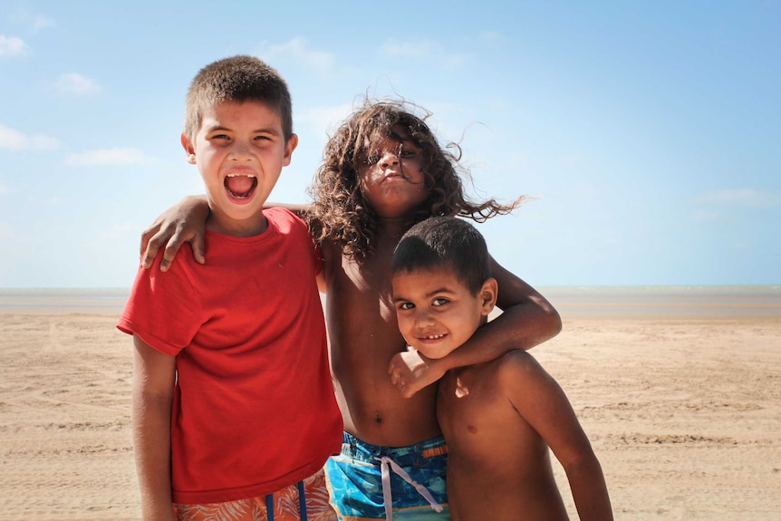 Three young aboriginal boys on Gunnamulla beach with their arms around each other.