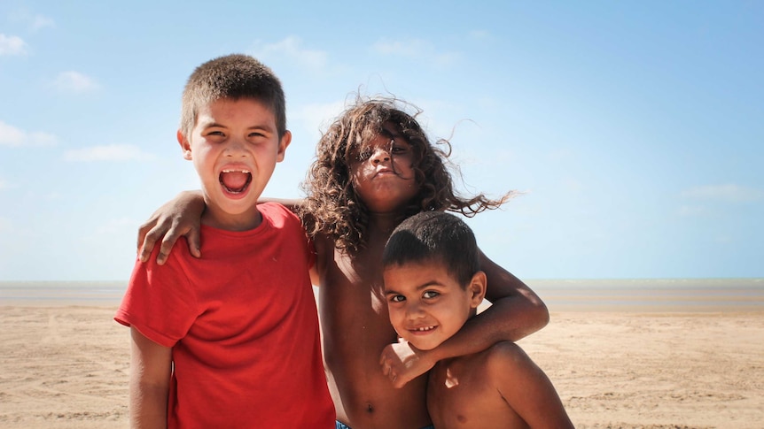 Three young aboriginal boys on Gunnamulla beach with their arms around each other.