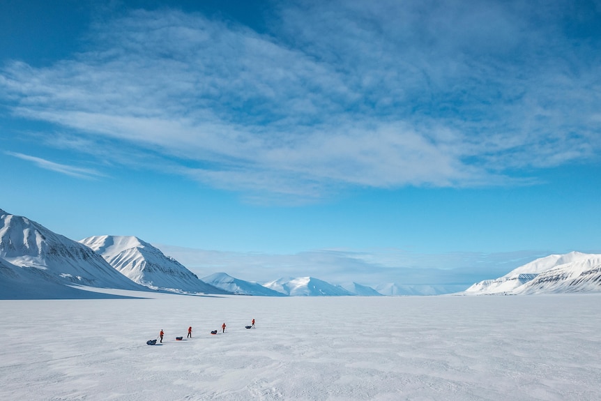 Brede landschapsfoto van mensen op ski's die over ijs in het Noordpoolgebied trekken