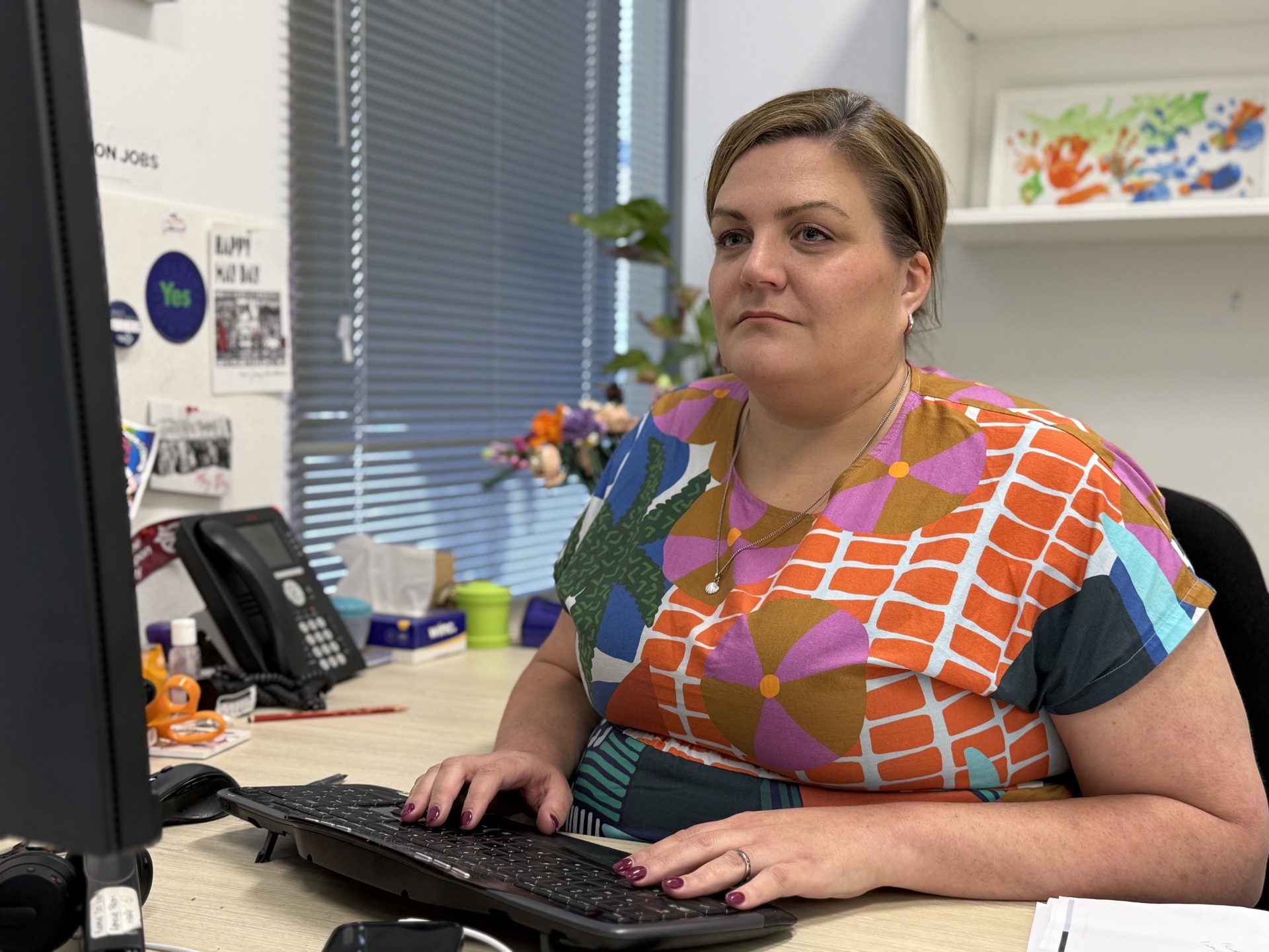 Emeline Gaske wears a brightly coloured and patterned outfit and sits at a desk.