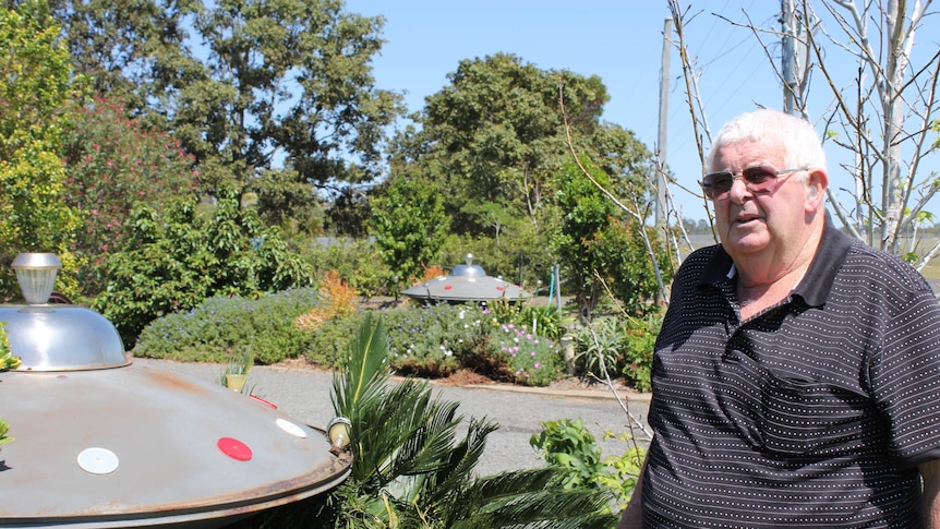 A man stands in his garden with two UFO sculptures in the background
