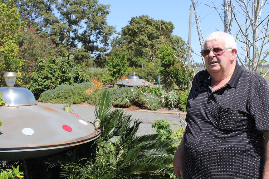 A man stands in his garden with two UFO sculptures in the background