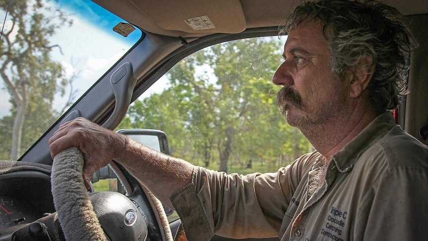 Freelance crocodile hunter Roger Matthews at the wheel of his car, driving through a cattle station.