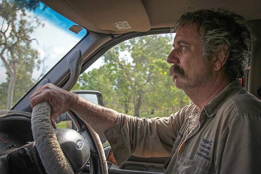 Freelance crocodile hunter Roger Matthews at the wheel of his car, driving through a cattle station.