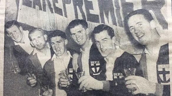 Black and white photograph shows footballers celebrating with a pennant.