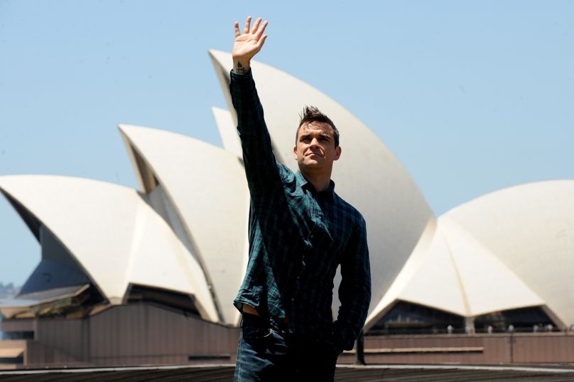Pop star Robbie Williams raises his arm in the air as he stands outside the Sydney Opera House.