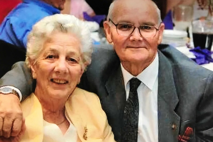 Mrs Jackson sits at a table smiling with a man who has his arm around her.