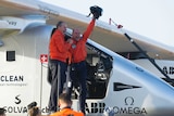 Bertrand Piccard and Andre Borschberg stand in the Solar Impulse 2 cockpit, celebrating.