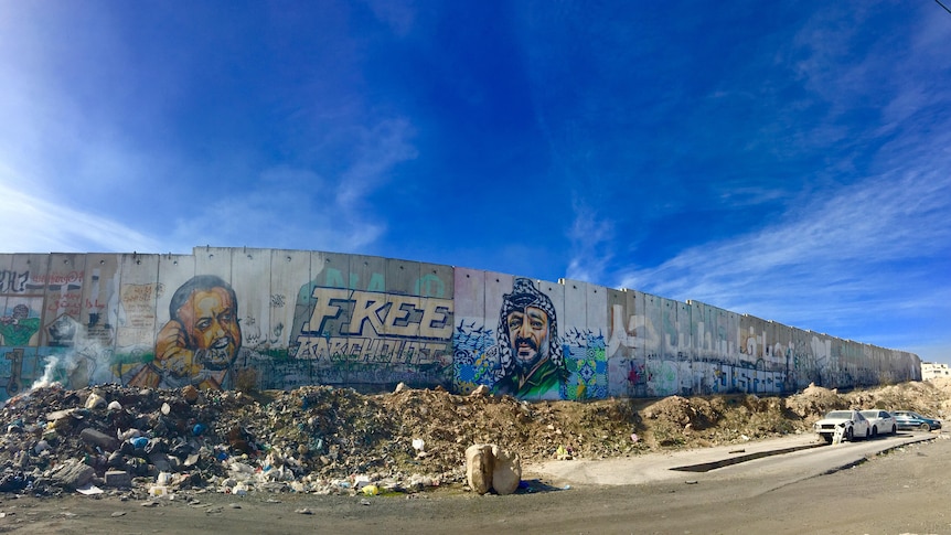 Graffitit on a wall says "Free Barghouti" next an image of a Palestian man's face, his raised hands handcuffed