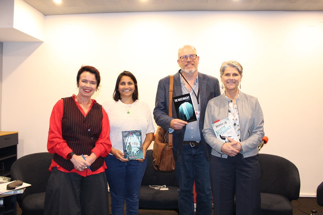 Four people standing in a row, three holding their novels and looking proud. All beaming. Names in caption