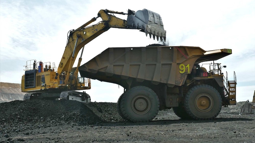 A truck is loaded with coal by a mine worker in a bob cat.