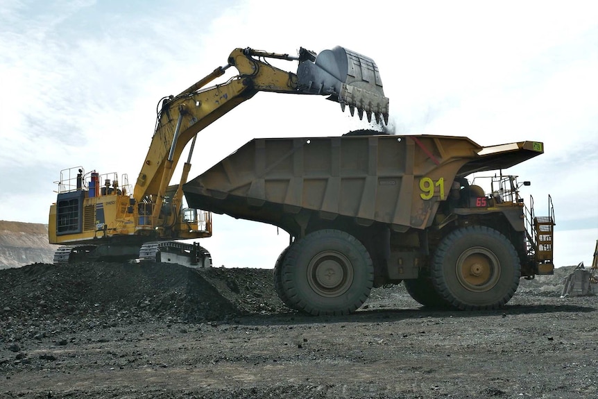A truck is loaded with coal by a mine worker in a bobcat.