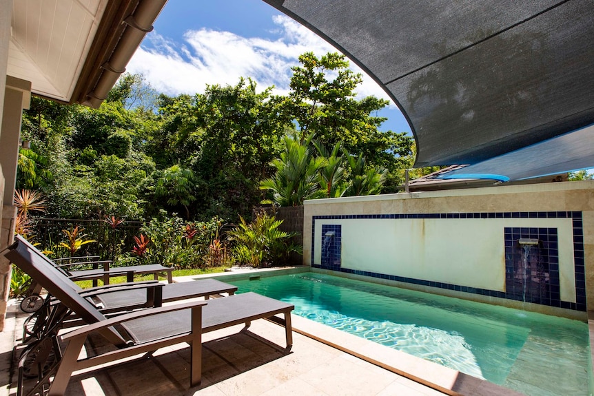 Lounge chairs sit beside a pool in a sunny but shaded courtyard.