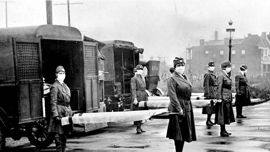 Members of the Red Cross Motor Corps (women in uniform and face masks) pose for a portrait with stretchers and ambulances