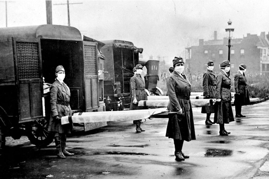 Members of the Red Cross Motor Corps (women in uniform and face masks) pose for a portrait with stretchers and ambulances
