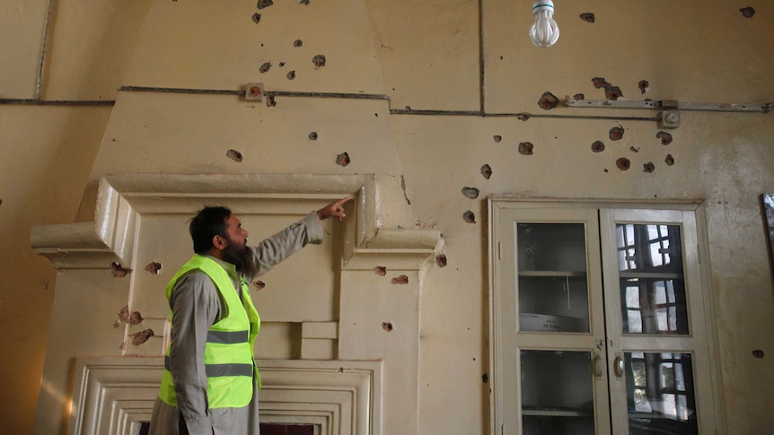 A man points at bullet holes in a wall.