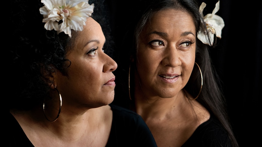 Sisters Vika and Linda Bull stare into the distance against a pitch black background