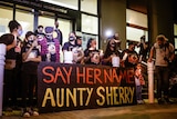 Protesters hold candles next to a sign that says "say her name Aunty Sherry".