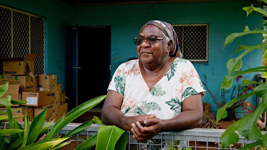 an aboriginal woman wearing sunglasses stands outside her house