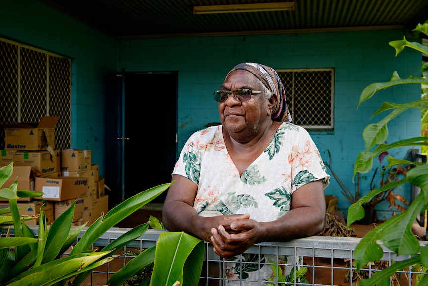 an aboriginal woman wearing sunglasses stands outside her house