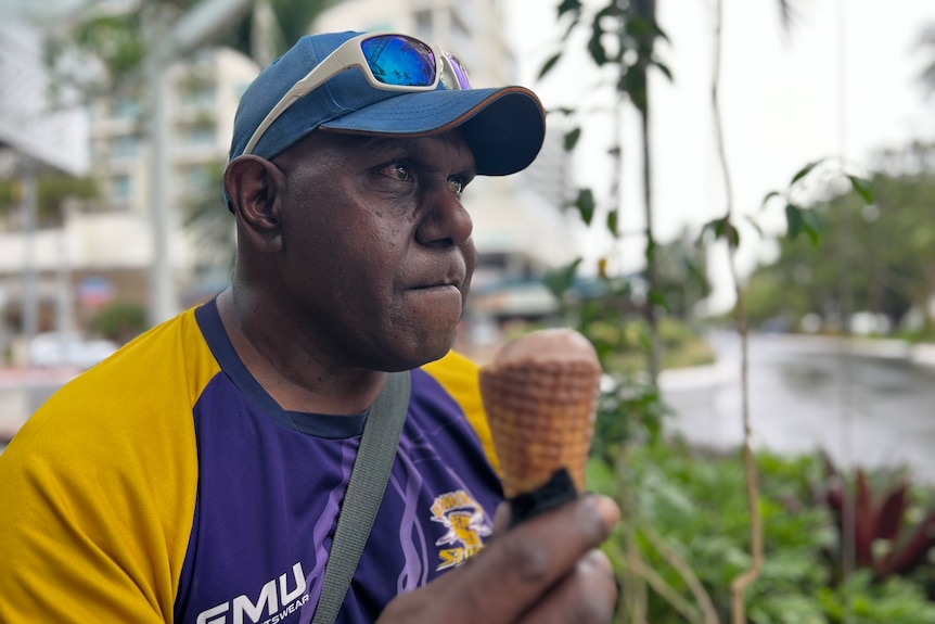A man wearing a hat eating an ice-cream.