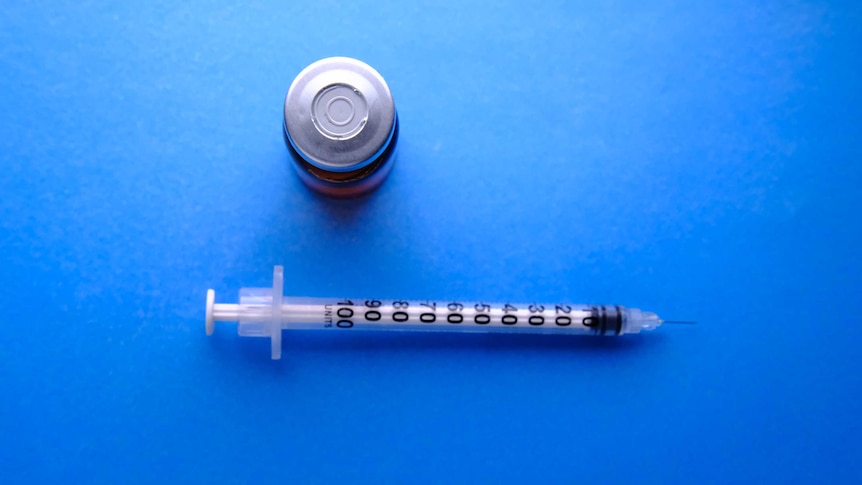 A syringe and bottle against a blue background.