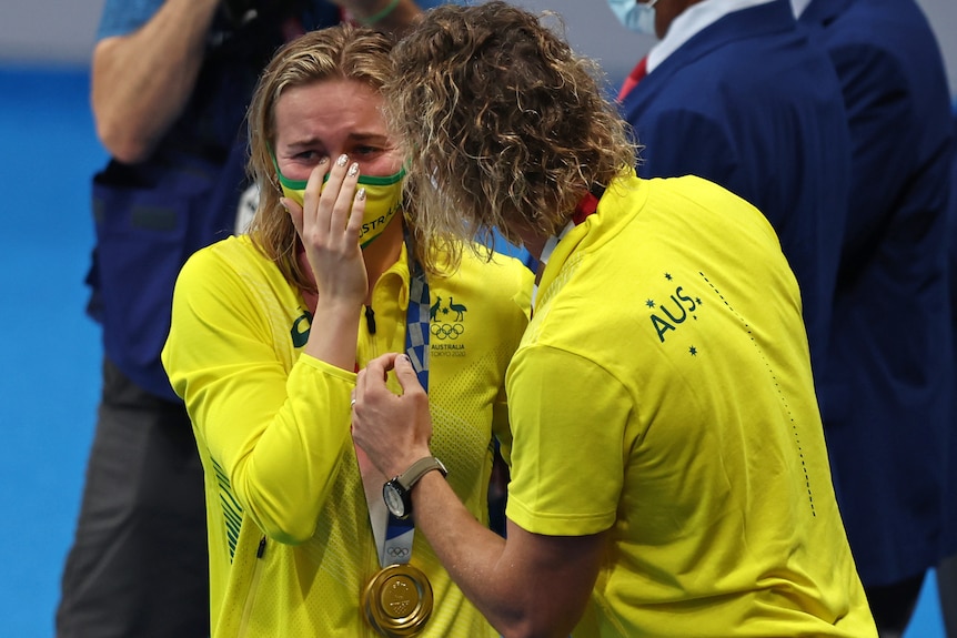 Dean Boxall consuela a Ariarne TItmus llorando.  Una medalla de oro está alrededor de su cuello.