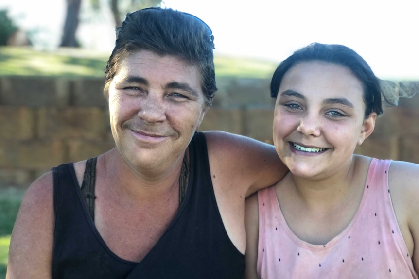 A mother and daughter sit in the shade under a tree in Broome