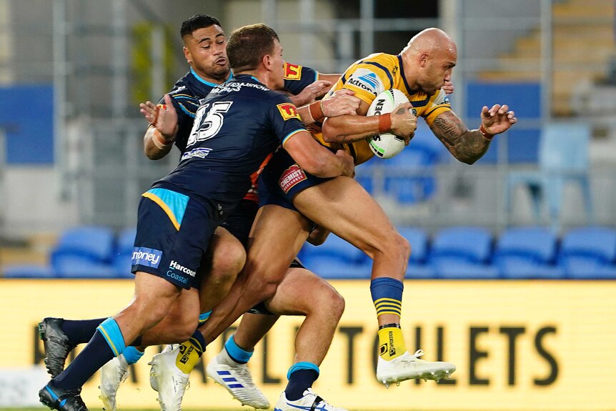 Parramatta Eels NRL player Blake Ferguson in yellow is tackled by two Gold Coast players ins dark blue.