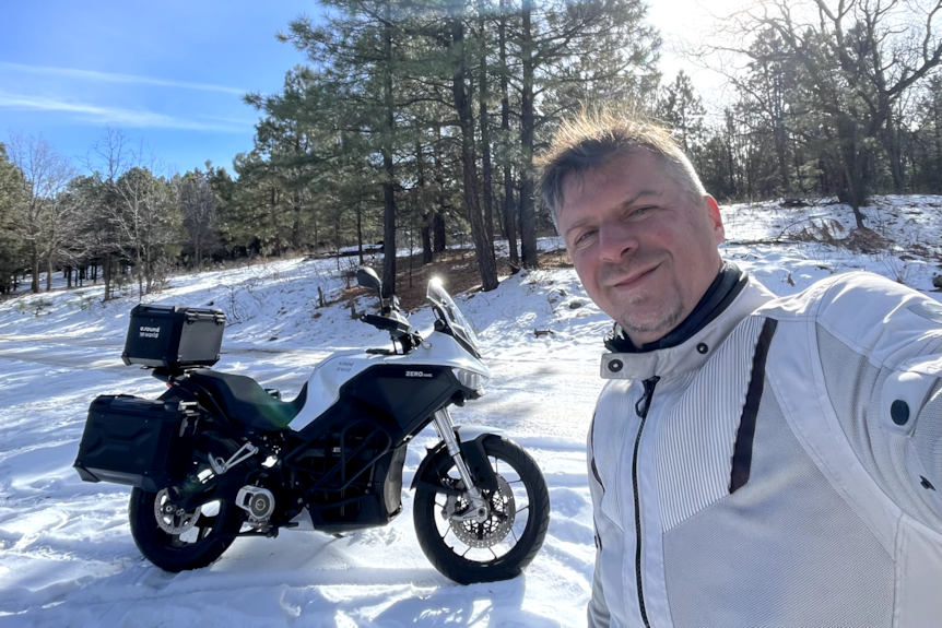 A man with a motorcycle parked in a snowy forest