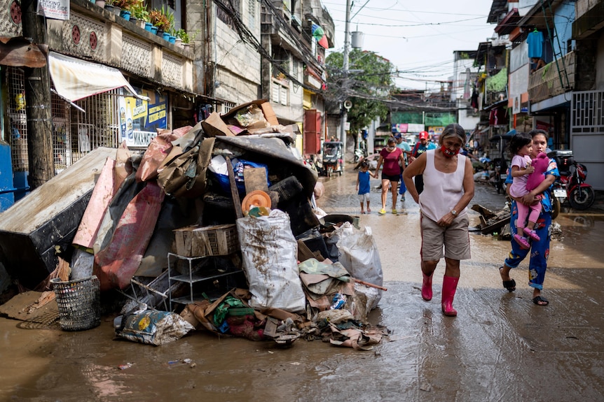 Residents walk past debris staked into a pile on a muddy road as a clean up from a flood begins.