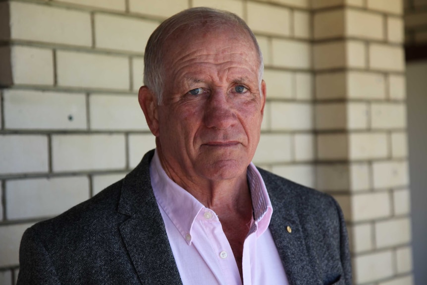 Head and chest shot of former ARU Board member Geoff Stooke standing in front of a cream bricked building