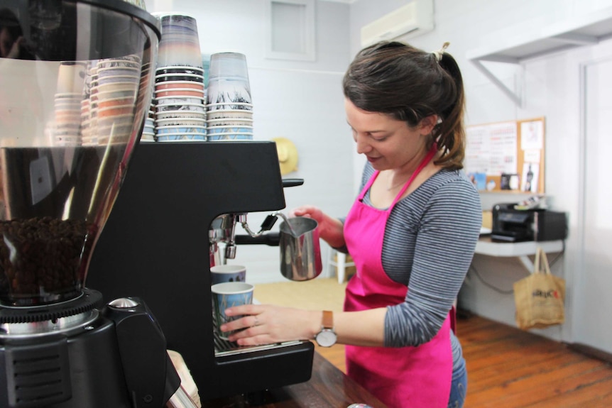 A woman in a pink apron making a coffee at a coffee machine.