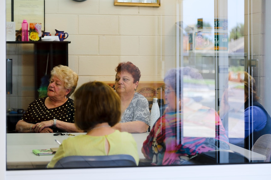 Through glass, you can see a group of casually dressed people meeting around a table inside an office