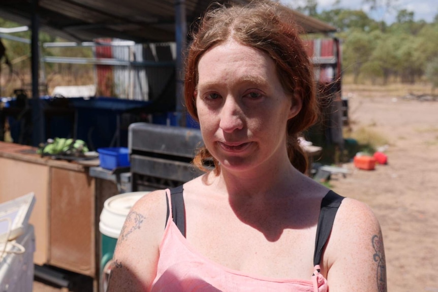 A women wearing a pink top stands near a shed