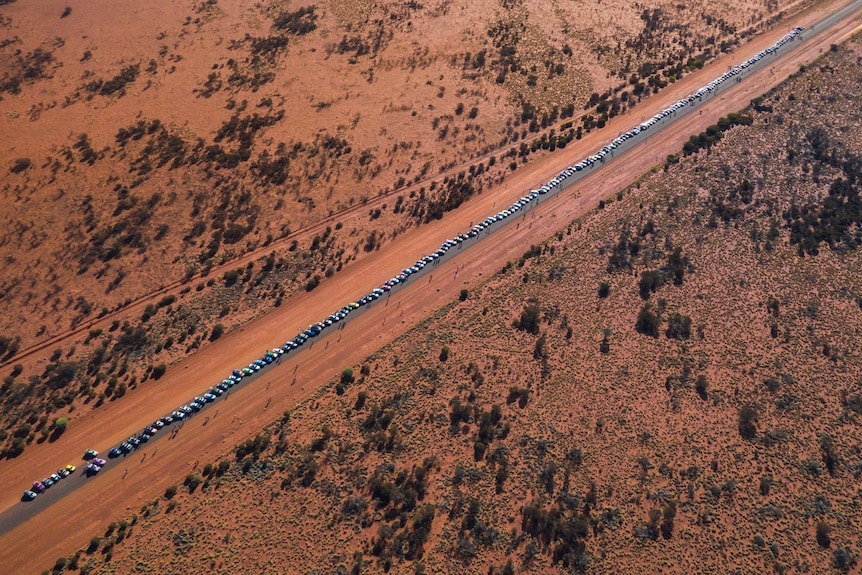 An aerial shot of a long line of cars travelling through the outback.