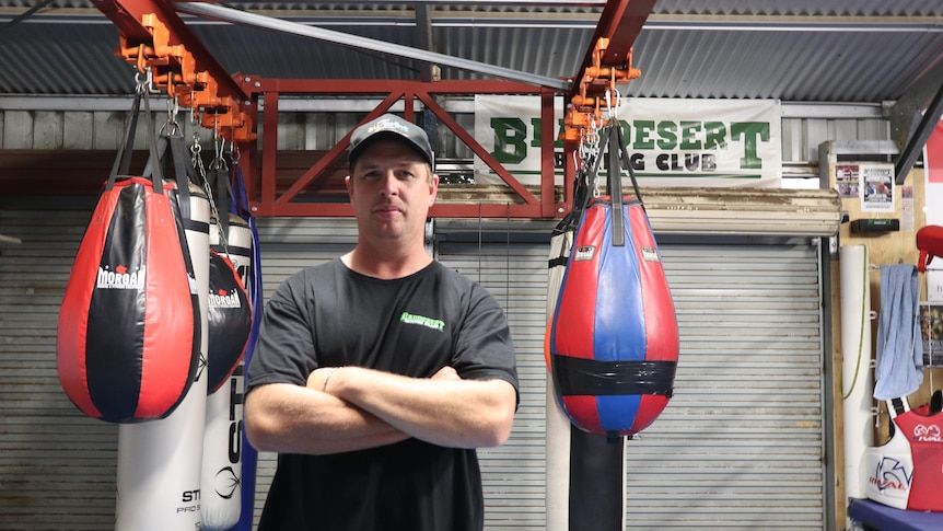 Justin O'Leary stands in front of boxing bags with arms folded.