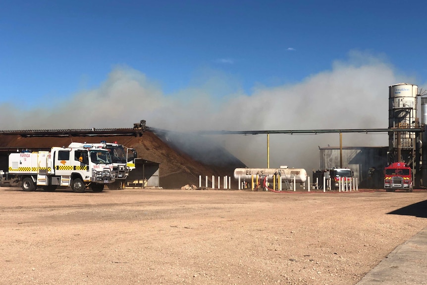 A CFS truck alongside a smoking pile of almond husks next to a processing facility.