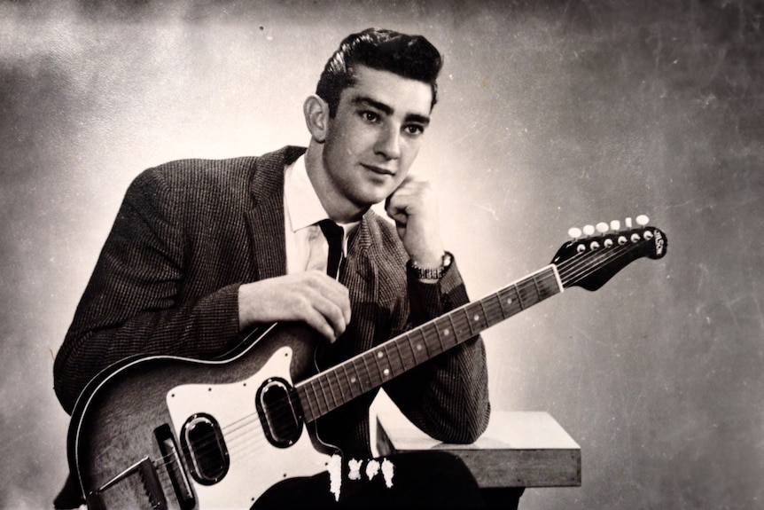 A young musician with a slick pompadour hairstyle poses with his electric guitar