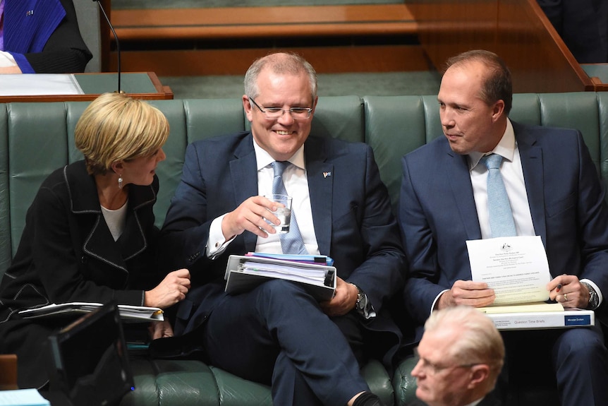 Scott Morrison smiles as Julie Bishop and Peter Dutton turn towards him to speak.