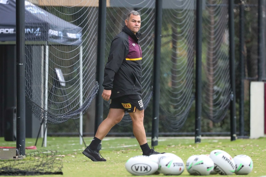 A middle-aged man in sports kit, including shorts, looks pensively as he walks across a rugby field.