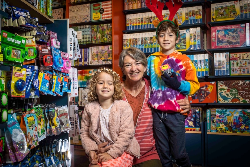 A grandmother sits next to her two grandchildren in a toy shop