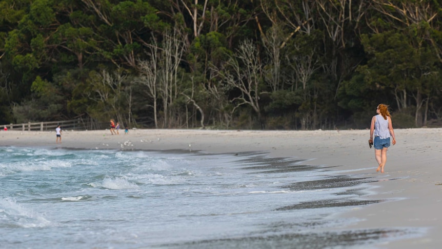 A woman walks along a white sand beach at Bonderee National Park