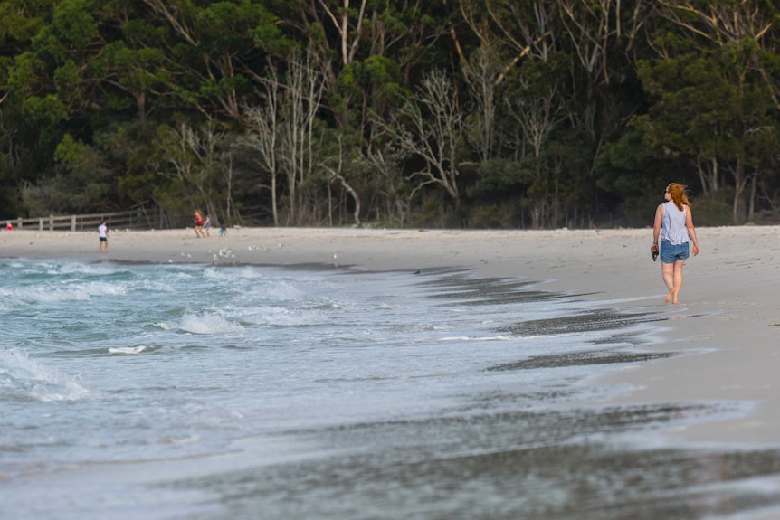 A woman walks along a white sand beach at Bonderee National Park