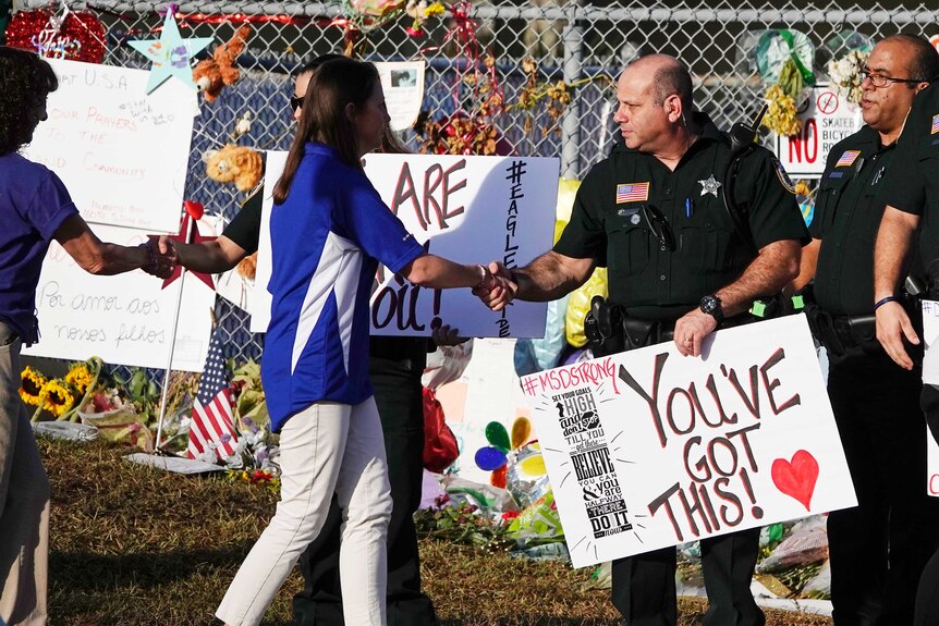 A lady shakes hands with a police officer, who is holding a supportive sign.