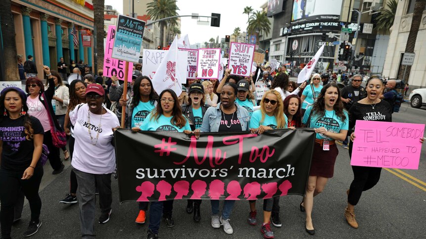 People march behind a banner with the words #Metoo