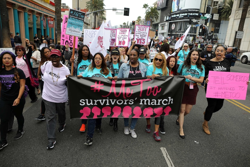 People march behind a banner with the words #Metoo