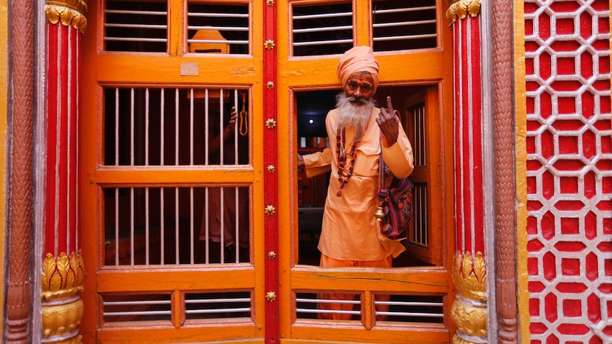 A man holds up his finger while stepping through a yellow, orange and gold doorway